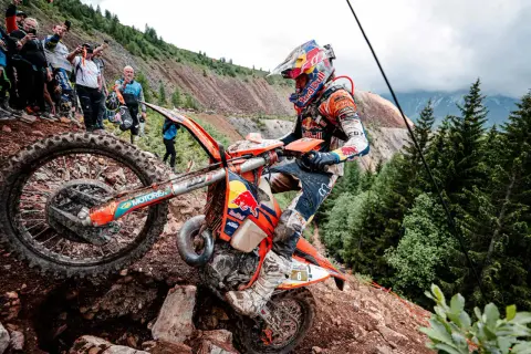 Motocyklista walczy z kamienistym podjazdem podczas Erzberg Rodeo. Widzowie obserwują zmagania na stromym zboczu.