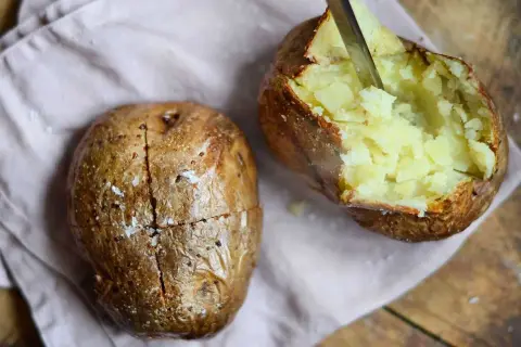 Perfekt bakad potatis i airfryer, en är uppskuren och visar det fluffiga inkråmet. Saltkorn glittrar på den gyllene ytan.