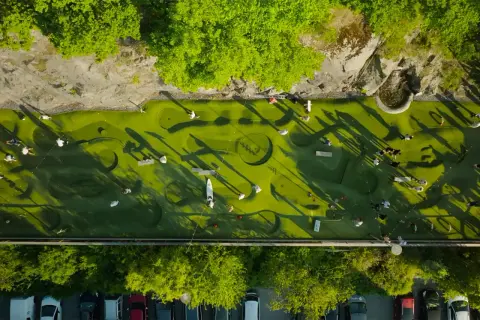 Folk spelar minigolf i Nacka Strand. En grön bana med hinder och skuggor från träden.