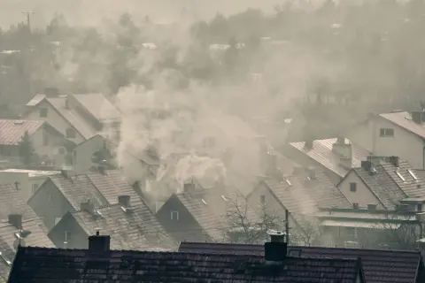 Dym wydobywający się z kominów domów na tle mglistego krajobrazu.