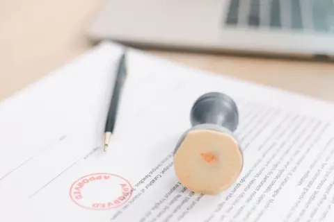 Długopis i pieczątka "APPROVED" na dokumencie. To symbol skutecznej windykacji i finalizacji spraw.