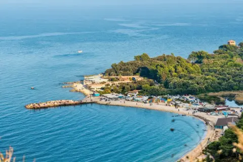 Una splendida spiaggia delle Marche, con un molo affollato, stabilimenti balneari e una pineta lussureggiante che si estende fino al mare.