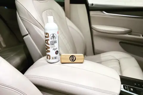 Zestaw do pielęgnacji jasnej skóry w samochodzie: butelka preparatu SWAG Leather Cleaner i drewniana szczotka. Idealne, by natłuścić skórę w samochodzie.