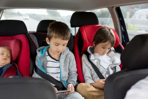 Im Auto mit 3 Kindern: Ein Baby schläft, die älteren Brüder sind mit ihren Handys beschäftigt.