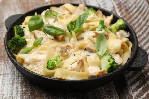 Pyszna potrawka z kurczaka z makaronem tagliatelle, brokułami i kremowym sosem, udekorowana świeżą bazylią.