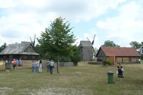 Skansen Osiek: drewniane budynki, wiatraki i ludzie spacerujący po trawie.