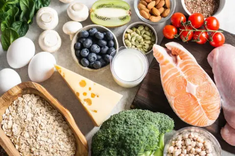 Vielfältige Lebensmittel für Muskelaufbau: Lachs, Hähnchen, Eier, Haferflocken, Beeren, Nüsse, Brokkoli, Käse und mehr.