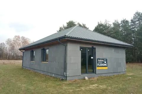 Gotowe domy pod klucz do 150 tys. zł. Nowoczesny, parterowy budynek z szarej cegły, z szarym dachem i dużymi oknami.