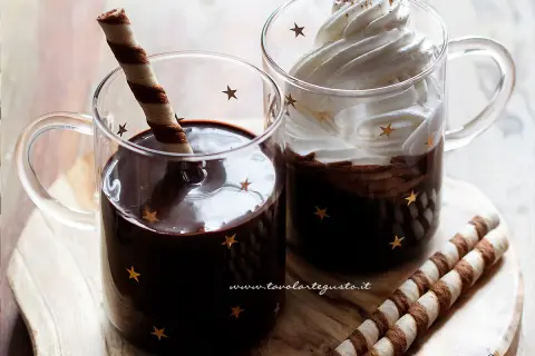 Due tazze di cioccolata calda con cacao e latte, una con panna e cacao, l'altra con un biscotto.