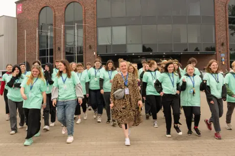 Grupa młodych ludzi w zielonych koszulkach z napisem "Szkoła w chmurze" idzie przed budynkiem.