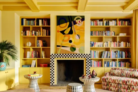 Ein Wohnzimmer in einem gelben Farb-Drenching-Stil mit Bücherregalen, einem Kamin und einem bunten Sofa.
