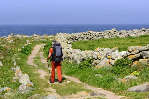 Pielgrzym z plecakiem idzie ścieżką wzdłuż kamiennego murku. Piękna trasa Santiago de Compostela nad oceanem.