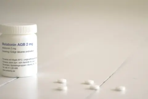 En burk med melatonin till barn, 2 mg, står på ett vitt bord. Några tabletter ligger utspridda framför.