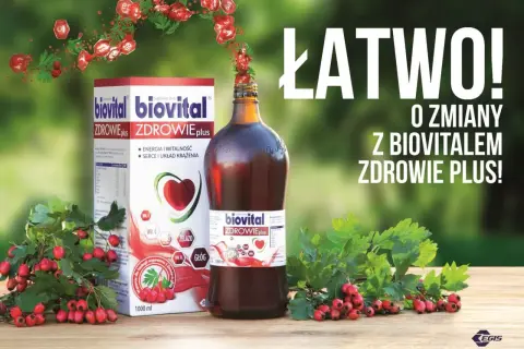 Biovital Zdrowie Plus – suplement diety z głogiem i witaminami. Pudełko i butelka na drewnianym stole, otoczone gałązkami z czerwonymi owocami.