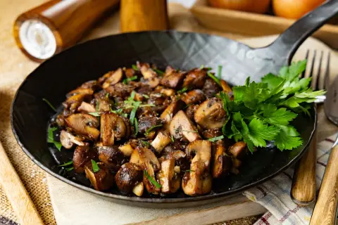 Gebratene Champignons in einer Pfanne, garniert mit frischer Petersilie. Ein köstliches Gericht, das zum Genießen einlädt.