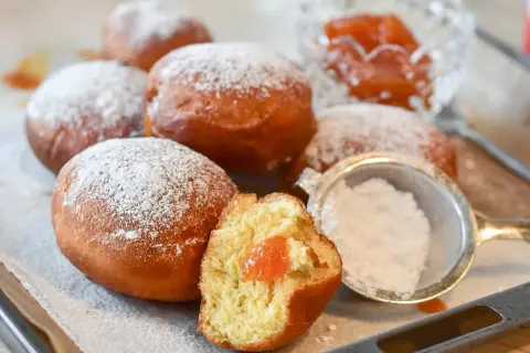 Rosquillas de naranja recién hechas, espolvoreadas con azúcar glas. Una está partida, mostrando su relleno de mermelada.