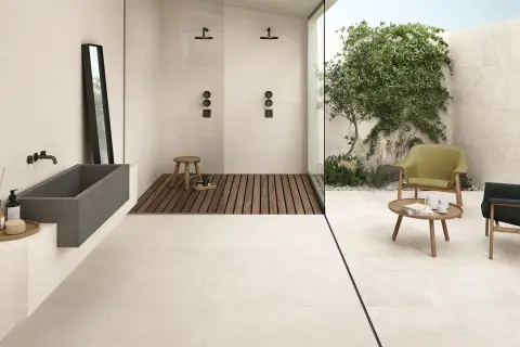 Bagno moderno con vasca in pietra, doccia a filo pavimento e un'area relax esterna. Il tipo di pavimentazione in gres porcellanato chiaro unifica gli spazi.