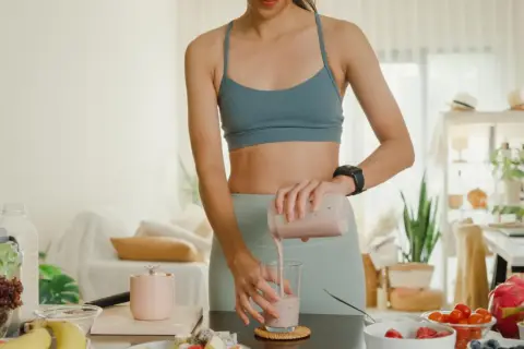 Frau mixt einen Smoothie, der zeigt, wie Proteinpulver beim Abnehmen helfen kann. Gesunde Zutaten liegen bereit.