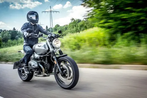 Motocyklista w kasku i kurtce jedzie drogą. Kask i kurtka to obowiązkowe wyposażenie motocykla, zapewniające bezpieczeństwo.