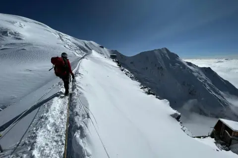 Bergsteiger auf dem Weg zum Mont Blanc besteigen, gesichert durch ein Seil, mit atemberaubendem Blick auf schneebedeckte Gipfel und Wolkenmeer.