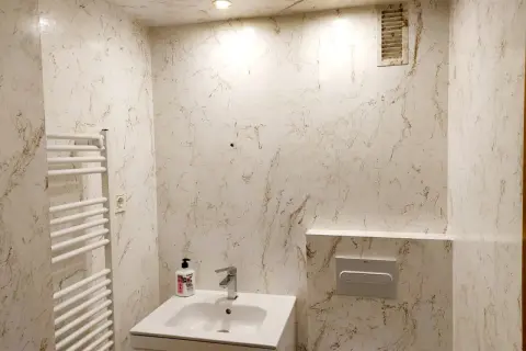 Elegante baño con paredes y techo acabados en resina epoxi con veteado marrón sobre blanco. Incluye lavabo, toallero y cisterna empotrada.