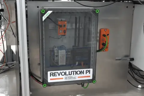 Wewnątrz przezroczystej obudowy widać system sterowania z napisem "REVOLUTION PI POWERED BY Raspberry Pi". To pokazuje, że raspberry co to za urządzenie, które zasila ten przemysłowy komputer.