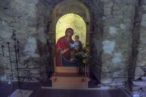 Ikona Matki Boskiej z Dzieciątkiem w kamiennej niszy cerkwi w Łopience. Obok świecznik.