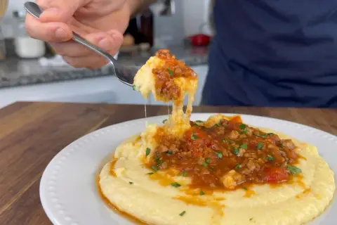 Un tenedor levanta una porción de polenta con tuco, mostrando su textura cremosa y la rica salsa de carne y tomate.