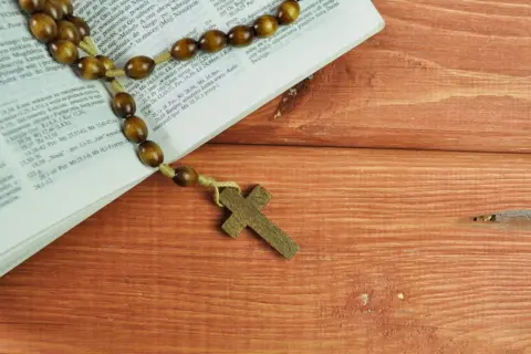 Różaniec na drewnianym stole obok Biblii, przypominający o 5 przykazaniach kościelnych.