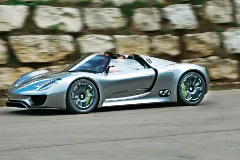 Srebrny Porsche 918 Spyder pędzi po drodze, z kierowcą za kierownicą.