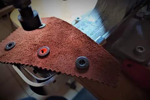 Zbliżenie na narzędzie do nabijania zatrzasków na skórzanym materiale.
