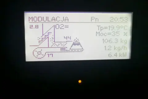Wyświetlacz pieca Kostrzewa z ustawieniami: modulacja, O2, temperatura, moc, waga paliwa, podajnik i moc grzewcza. System fuzzy logic optymalizuje pracę.