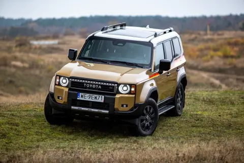 Złoty Toyota Land Cruiser z czarnymi dodatkami i relingami dachowymi stoi na trawiastym wzgórzu.