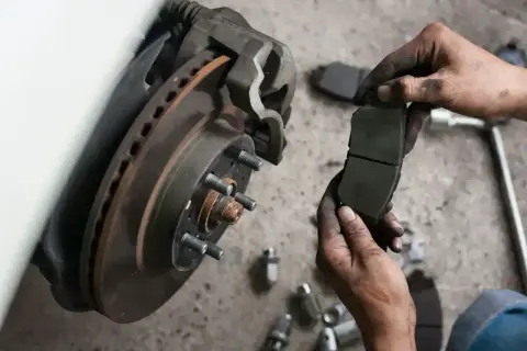 Mechanik trzyma zużyte klocki hamulcowe, zastanawiając się, co ile wymieniać klocki hamulcowe. W tle widać tarczę hamulcową.