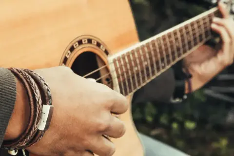 Dłoń z bransoletką gra na gitarze, tworząc dźwięki w tonacji c-dur.