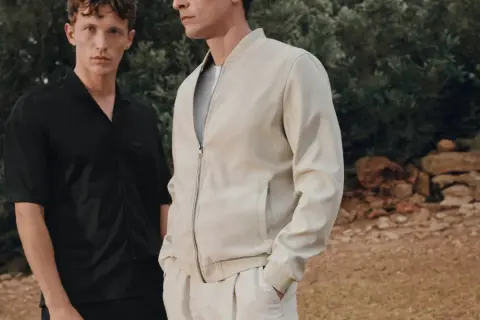 Zwei Männer im lässigen Party-Chic-Look: Einer trägt ein schwarzes Hemd, der andere eine cremefarbene Bomberjacke.