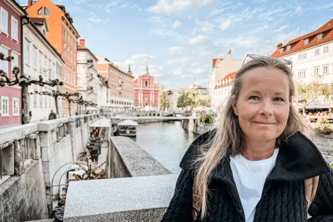 Kvinna ler vid floden i Ljubljana, Sloveniens huvudstad, med färgglada byggnader och en kyrka i bakgrunden.