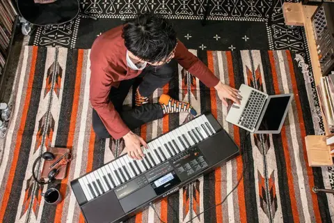 Mężczyzna gra na keyboardzie Casio, obok laptop i słuchawki.