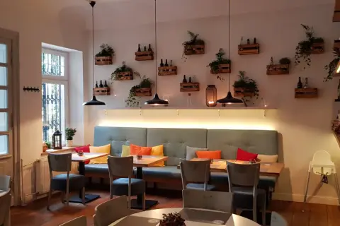 Przytulne wnętrze restauracji Nova Sopot z wygodnymi kanapami, drewnianymi skrzynkami z roślinami na ścianie i stylowymi lampami.