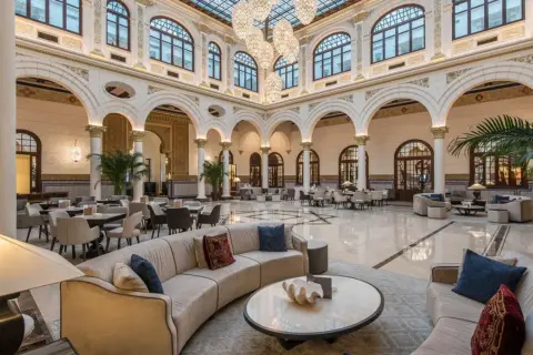 Elegante lobby del spa hotel Miramar, con sofás curvos, mesas y grandes lámparas de araña bajo un techo de cristal.