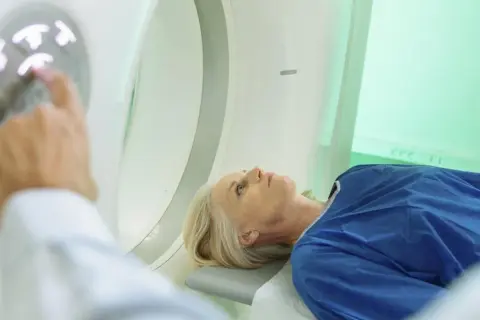 Pacjentka leży na stole do badania, a technik przygotowuje badanie tk.