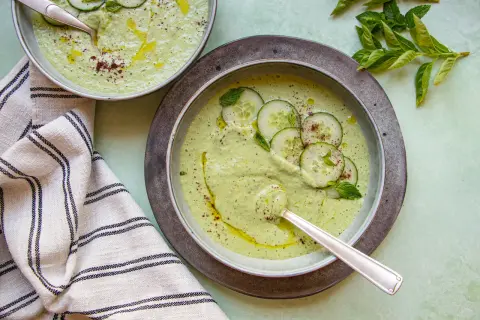 Deux bols de soupe froide aux concombres et menthe, arrosés d'huile d'olive et saupoudrés d'épices.