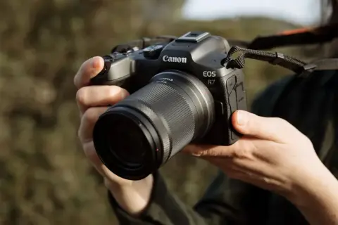 Mains tenant un appareil photo Canon EOS R7 avec un objectif. Prêt à capturer la beauté de la nature.