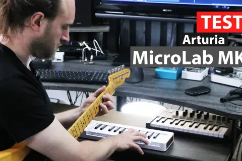 Mężczyzna gra na gitarze, obok niego leży biały midi keyboard Arturia MicroLab MK3.