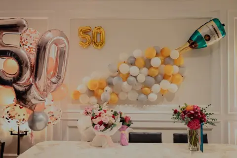 Pięćdziesiąte urodziny żony! Balony w kształcie cyfr 50, szampan i bukiety kwiatów tworzą radosną atmosferę.