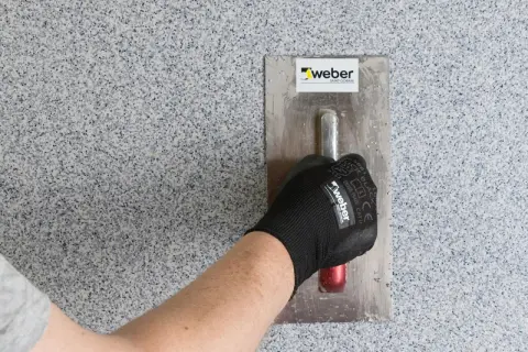 Nakładanie tynku mozaikowego w przedpokoju. Ręka w rękawicy Weber zacierająca ścianę.
