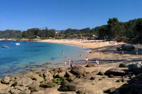 Gente disfrutando del sol y el mar en la Praia da Mourisca, con aguas cristalinas y arena dorada.