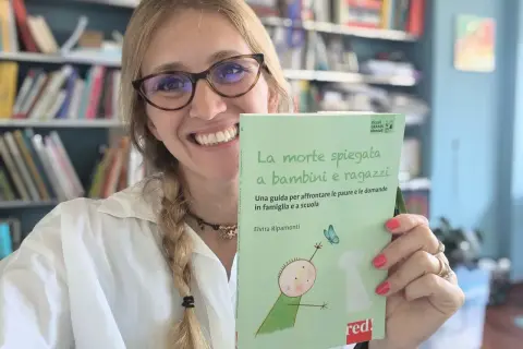 Donna sorridente con libro "La morte spiegata a bambini e ragazzi", affronta la paura di morire e lasciare i figli.