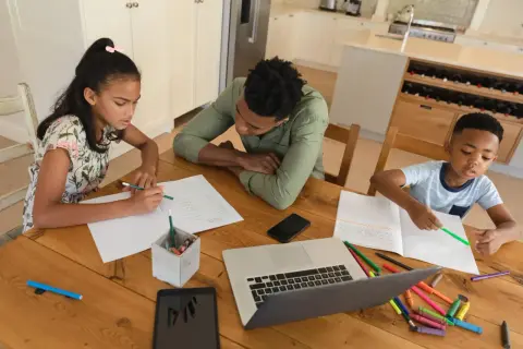 Familie lernt zu Hause. Ist Homeschooling in Deutschland erlaubt? Kinder schreiben und malen, Vater hilft.