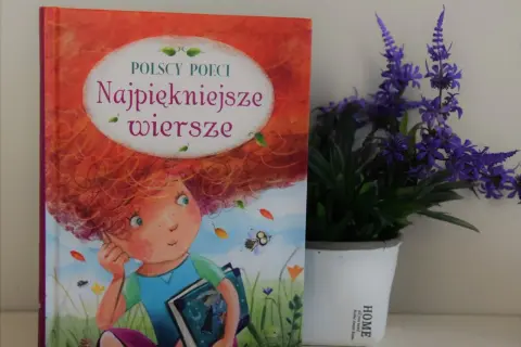 Książka "Najpiękniejsze wiersze polskich poetów" z ilustracją dziewczynki z rudymi włosami, obok doniczki z fioletowymi kwiatami.